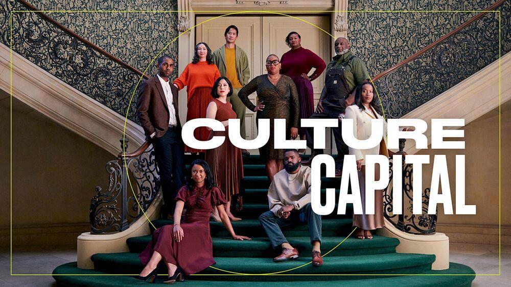 A group of people posed on a large stair case with emerald green carpet and intricate railings "Culture Capital" over the image.