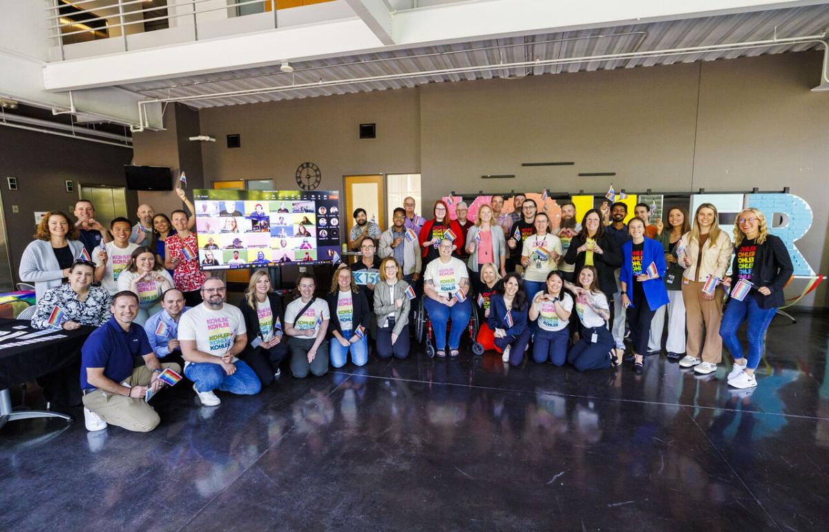 A group posed with a display. Many in matching rainbow shirts.