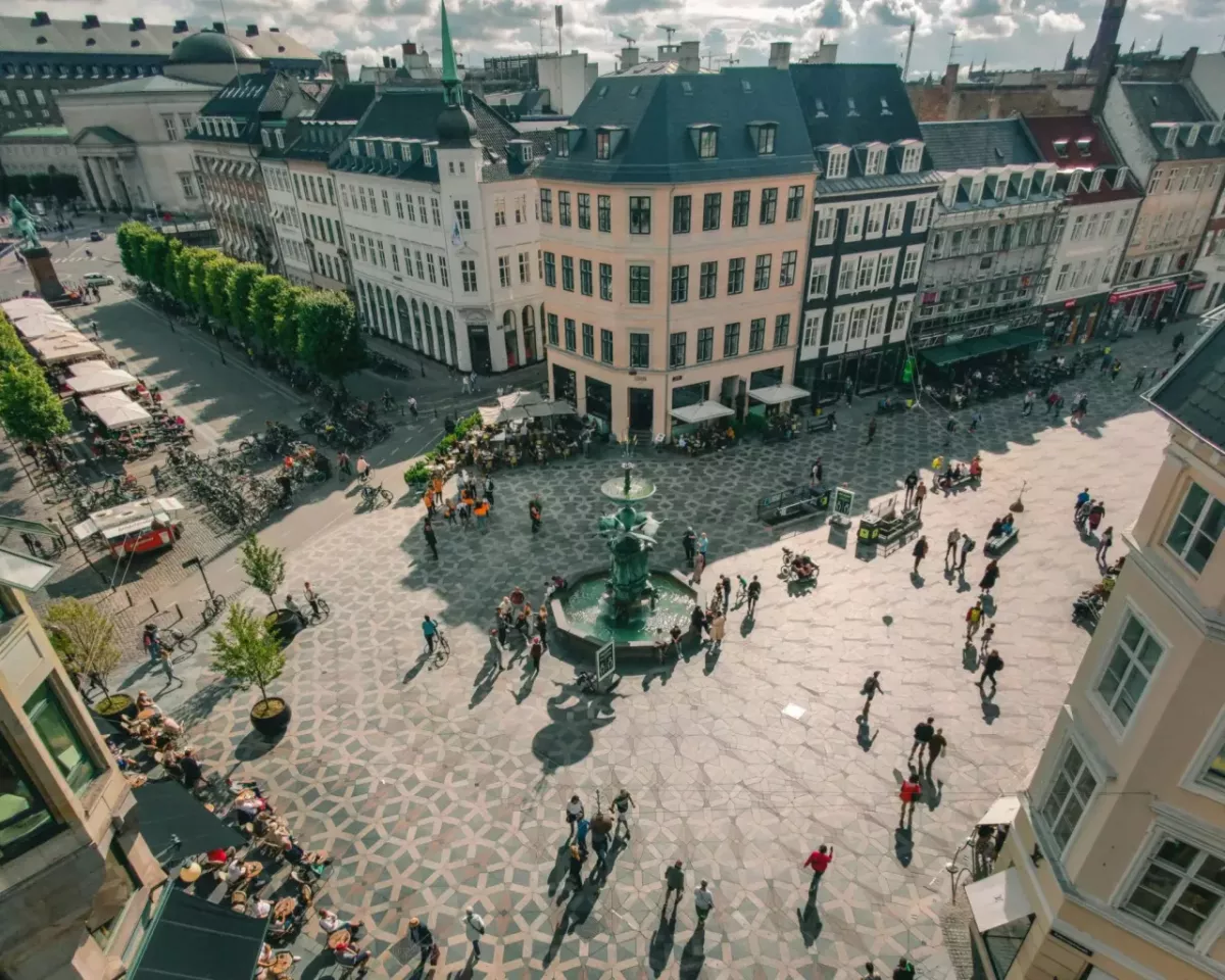 Aerial view of a city center full of pedestrians and bicycles. A fountain central to the street crossing.