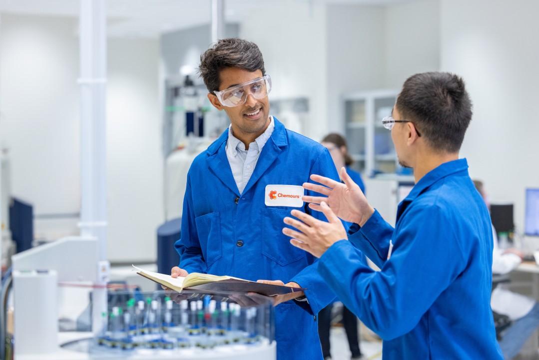 Two people wearing blue lab coats in a lab