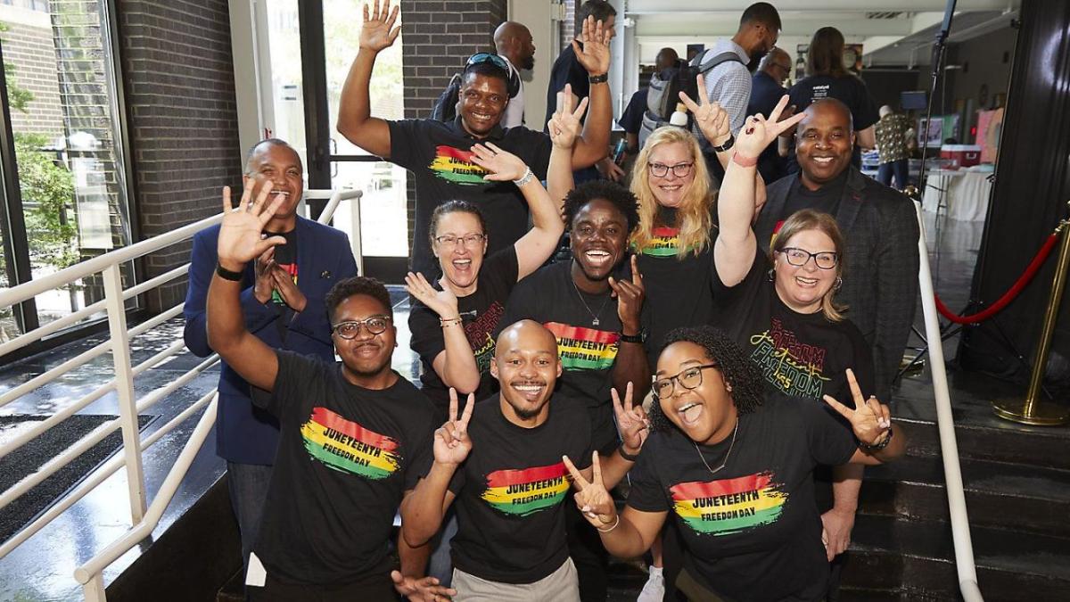 A group posed in matching "Juneteenth" shirts, giving peace-signs or raised hands.