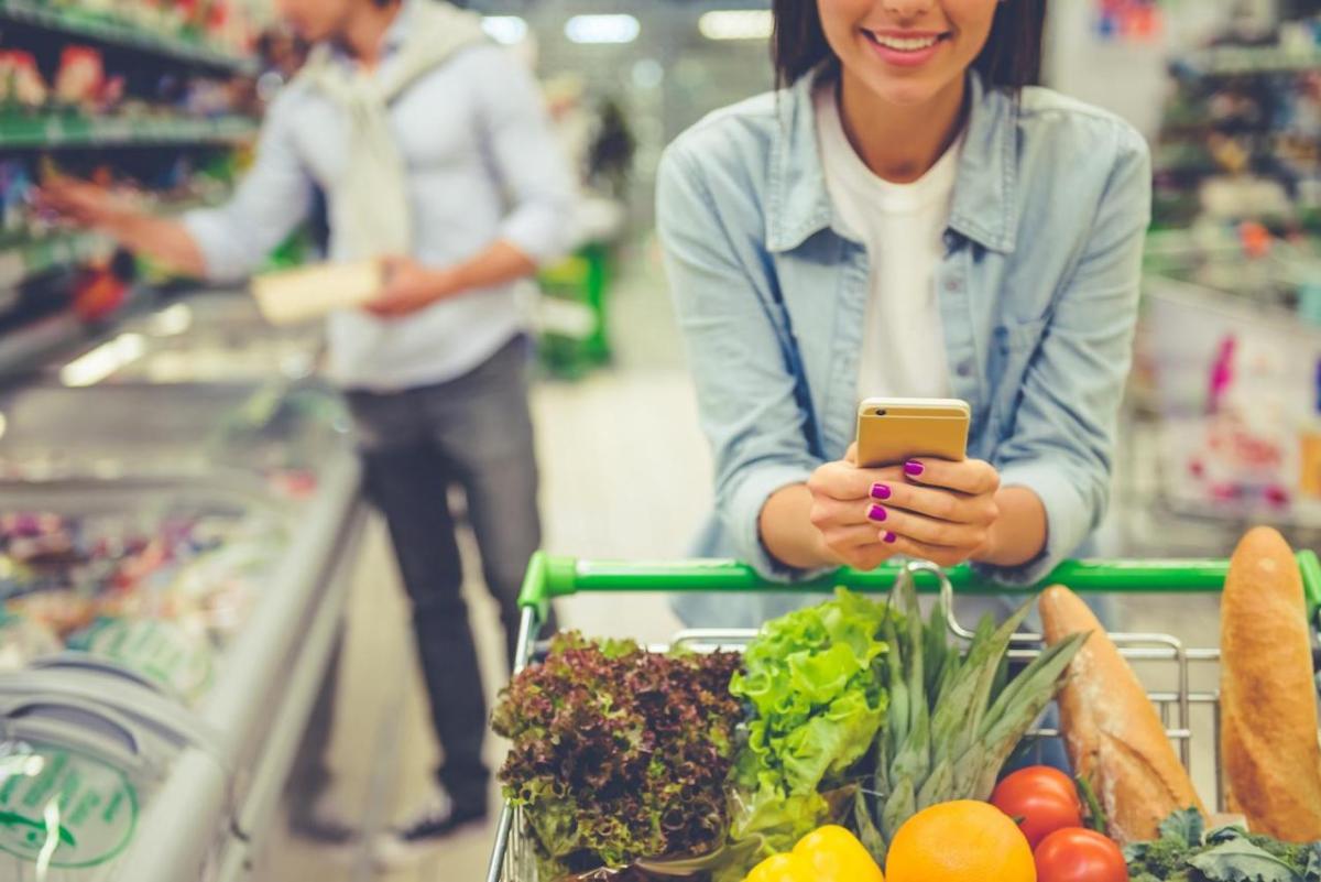 A couple shopping in a grocery store. One of them is consulting their phone.