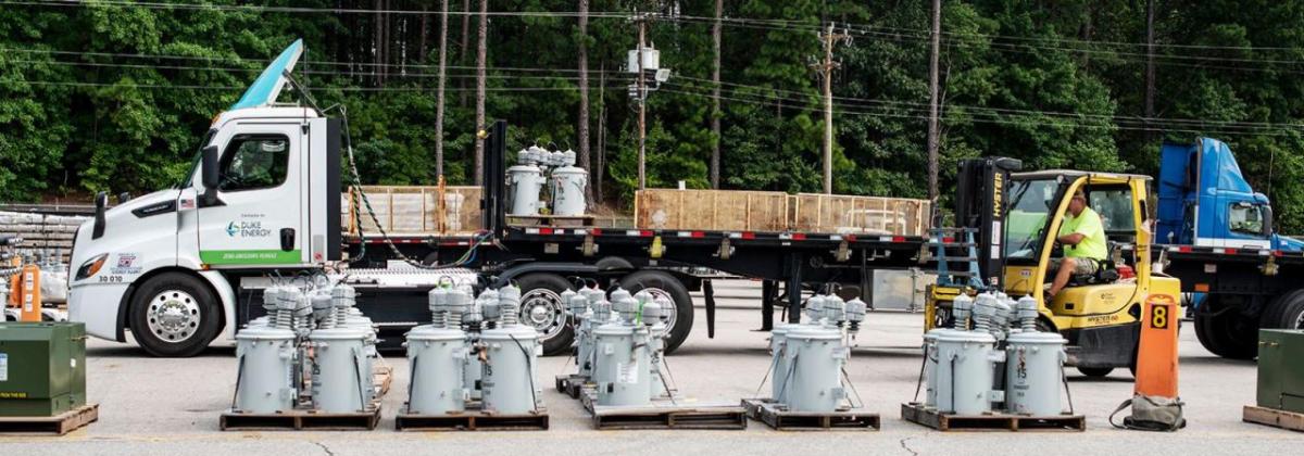 A semi truck in a parking area. Electrical equipment and a person in a forklift in front of it.