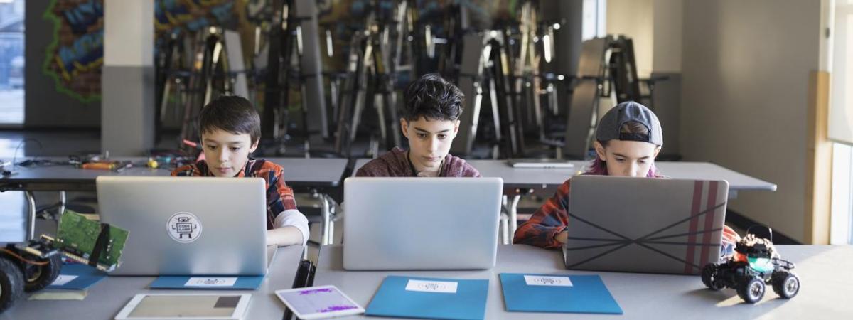 Three students at a shared table each with an open laptop.