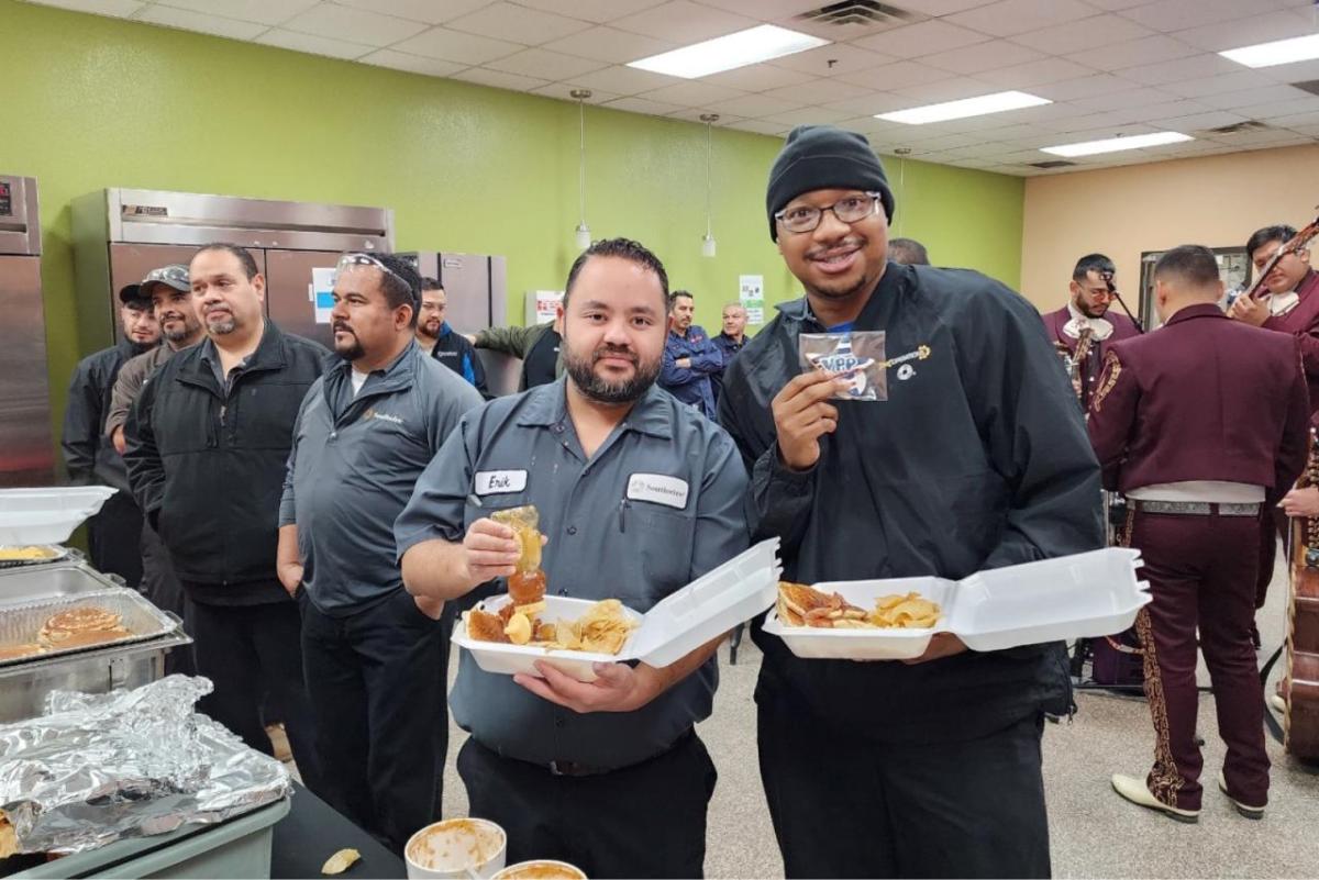 A roof full of employees, some in line for a buffet, two pose for the camera with containers of food.