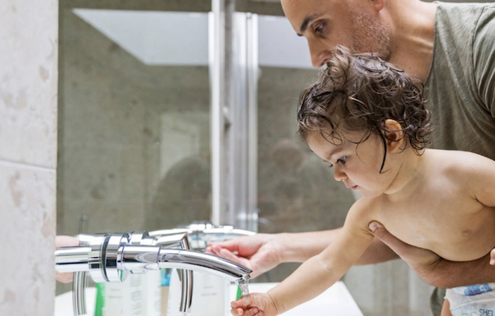 Man is holding a baby with his hand under a faucet.