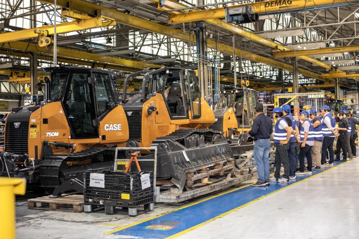 People stood wearing safety hats looking at tractors inside a factory