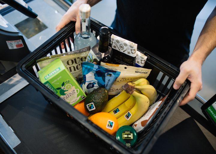 A basket of grocery items with the Fairtrade Mark, including oranges, bananas, tea, avocado, cocoa powder, and more. 