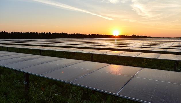 Long rows of solar panels, a rising sun inthe distance.