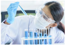 A person in protective lab gear looking at a small tube of blue liquid.