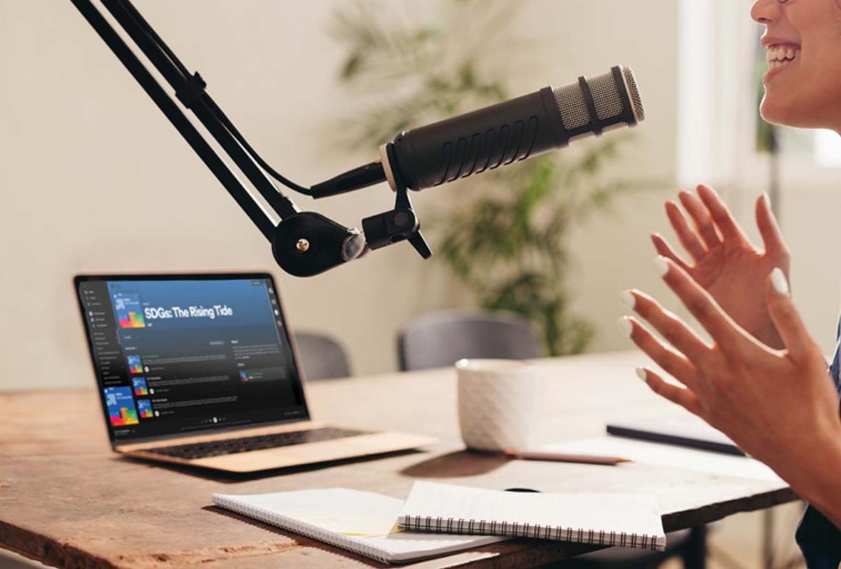 person speaking into microphone with laptop next to them on a desk