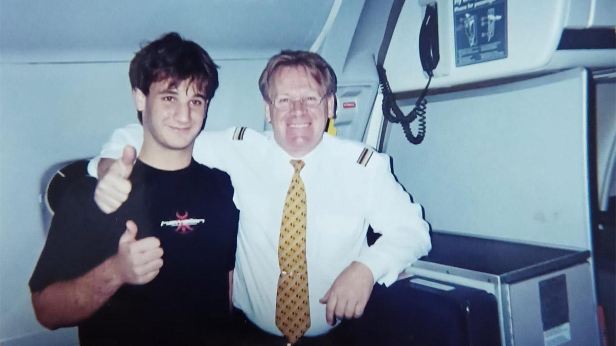 Two people stood next to each other smiling inside an aeroplane 