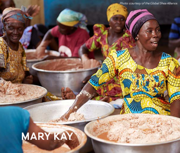 Women seated next to large metal bowls full of shea butter.