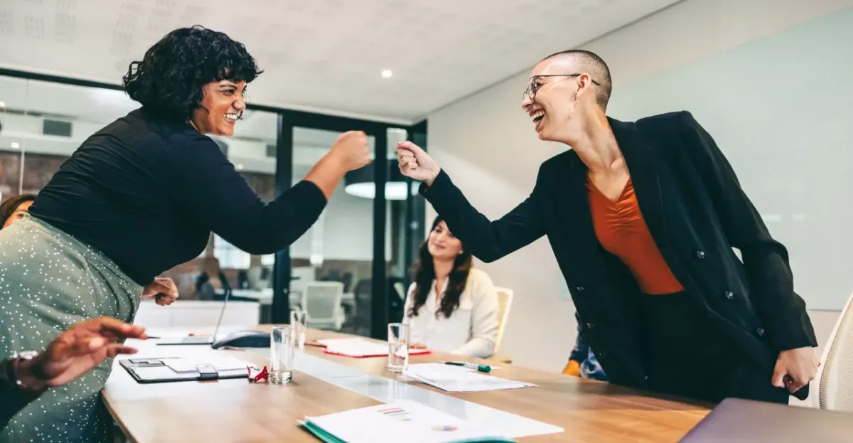 Two diverse colleagues smile and fist bump during a meeting, symbolizing support, inclusion, and positive workplace culture.
