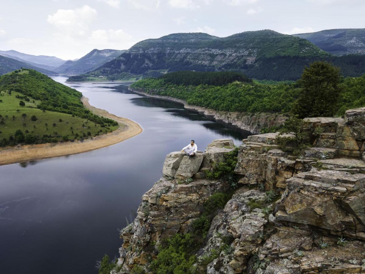 A person seated on a tall rock overlooking a winding river.