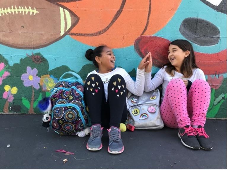 Photo of two young girls seated and giving a high five.