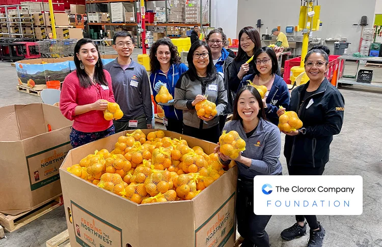 Smiling group of people standing around a pallet of oranges