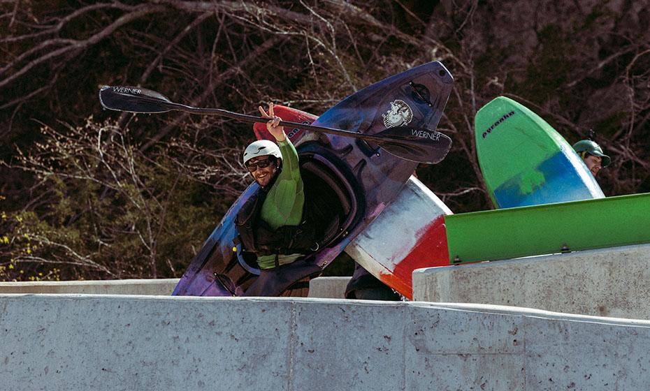 Person carrying a kayak while waving