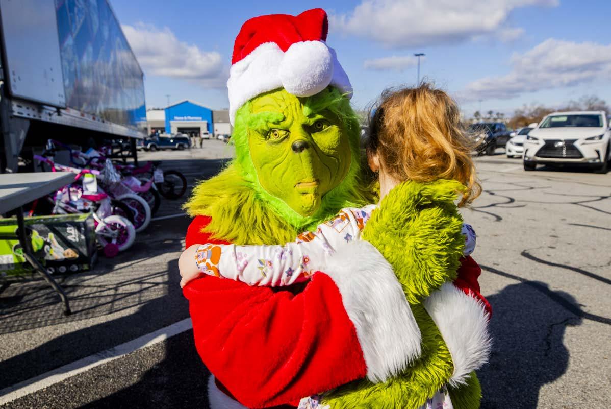 A person dressed as the Grinch hugging a child outside