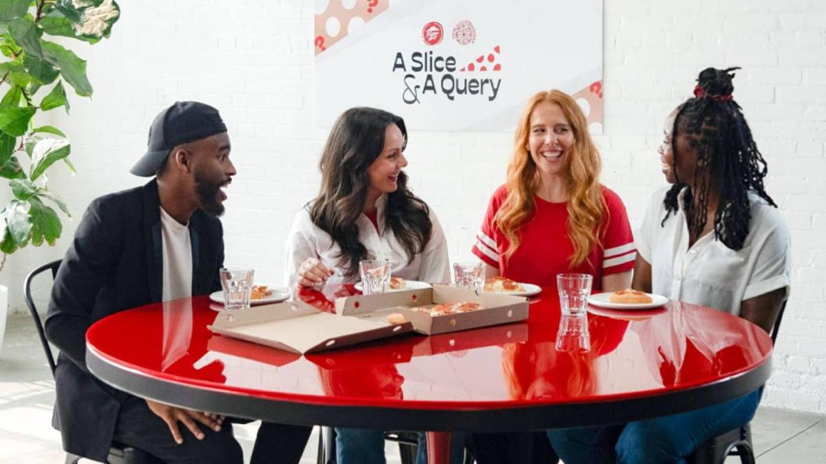 four people sat around a red table eating pizza