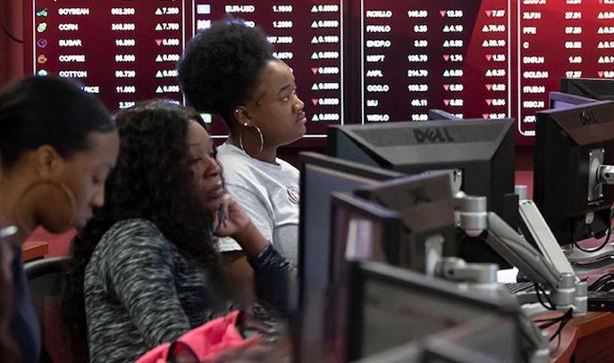 Female people of color sit in a classroom behind computer screens.