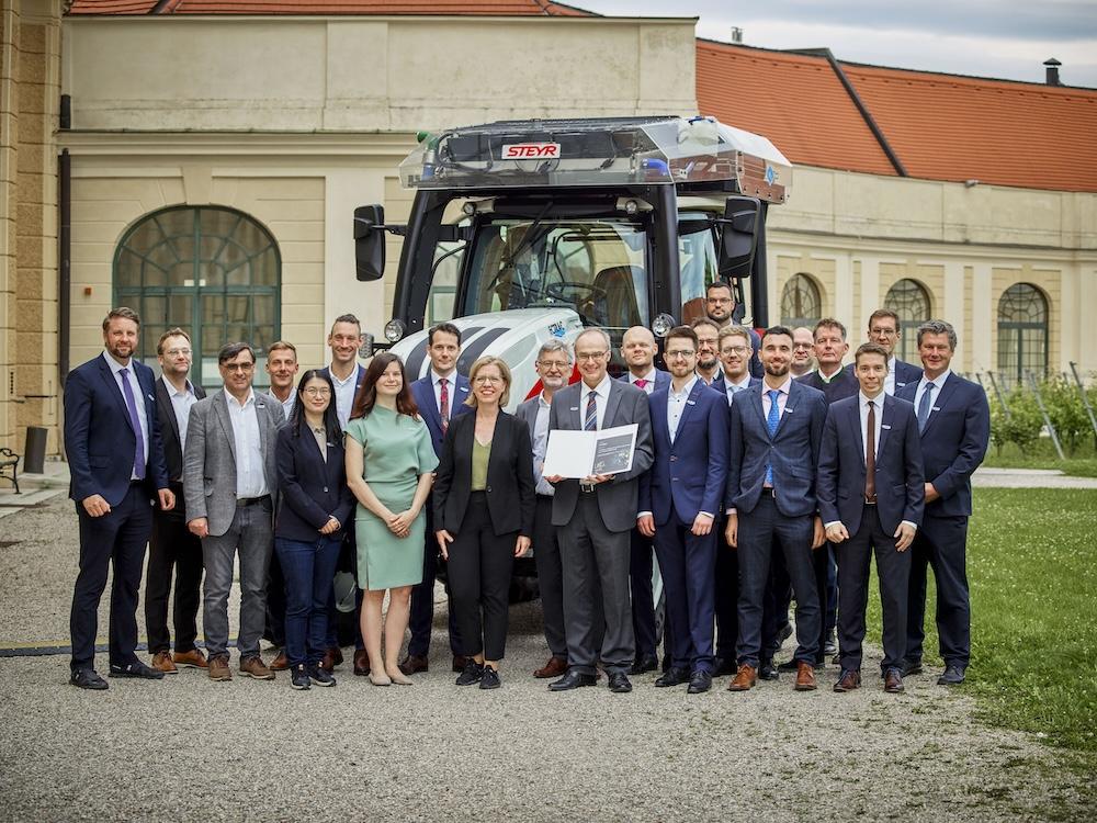 Group of people in formal attire standing outside in front of large tractor