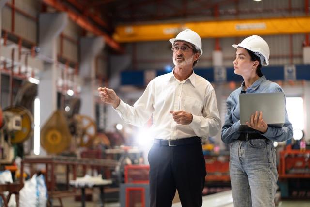 Two people wearing hard hats speaking in a workshop