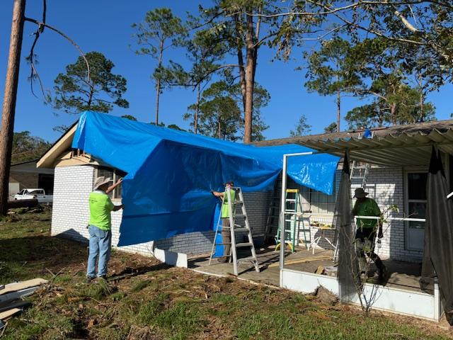 Volunteers putting a tarp over a storm damaged home