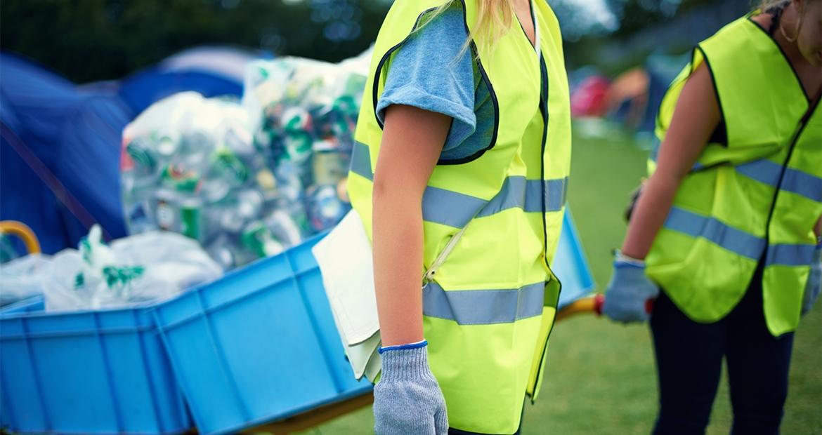 two people wearing reflective vests carrying carts full of recycling