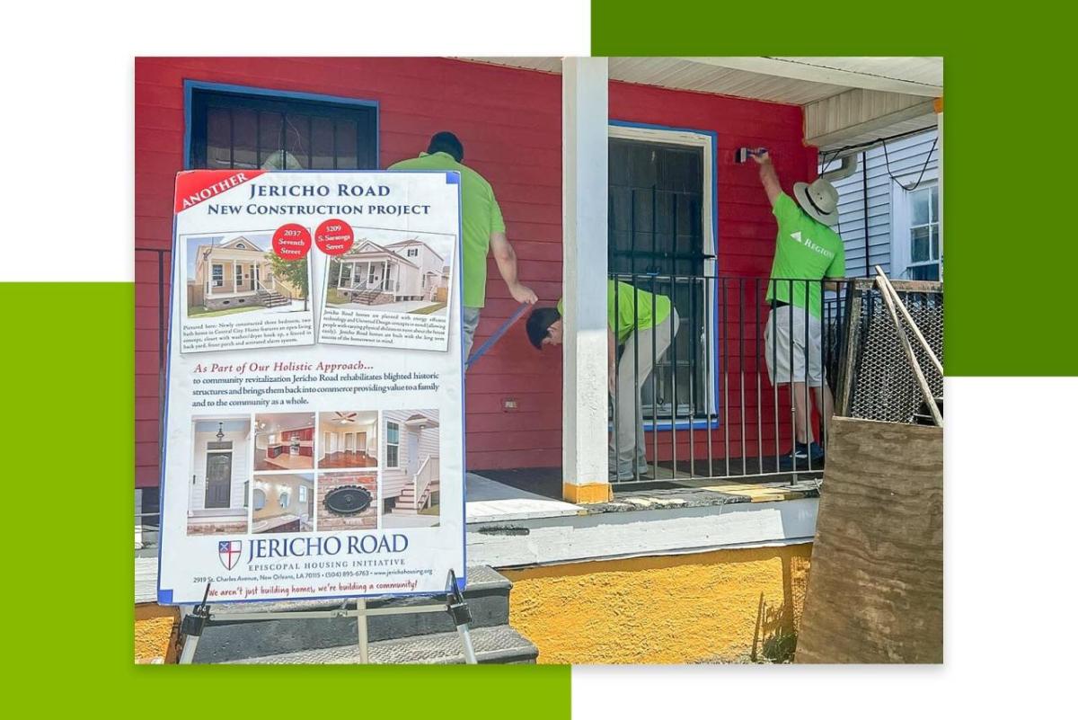 Volunteers painting a house red. A board with information in front of them.