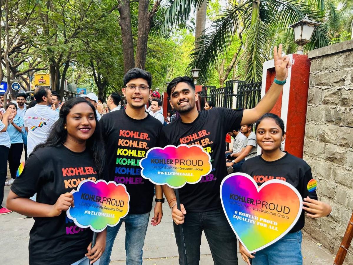 A group posed outside holding rainbow colored, shaped boards "Kohler Proud"