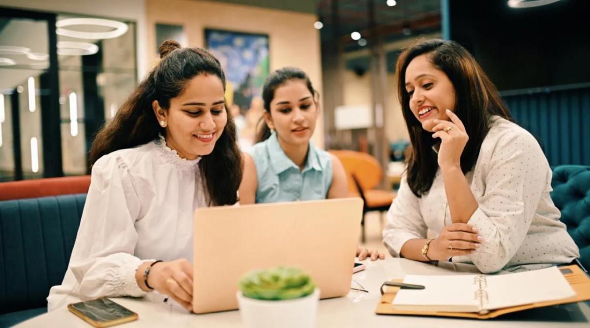 Three people sat at a table looking at a laptop