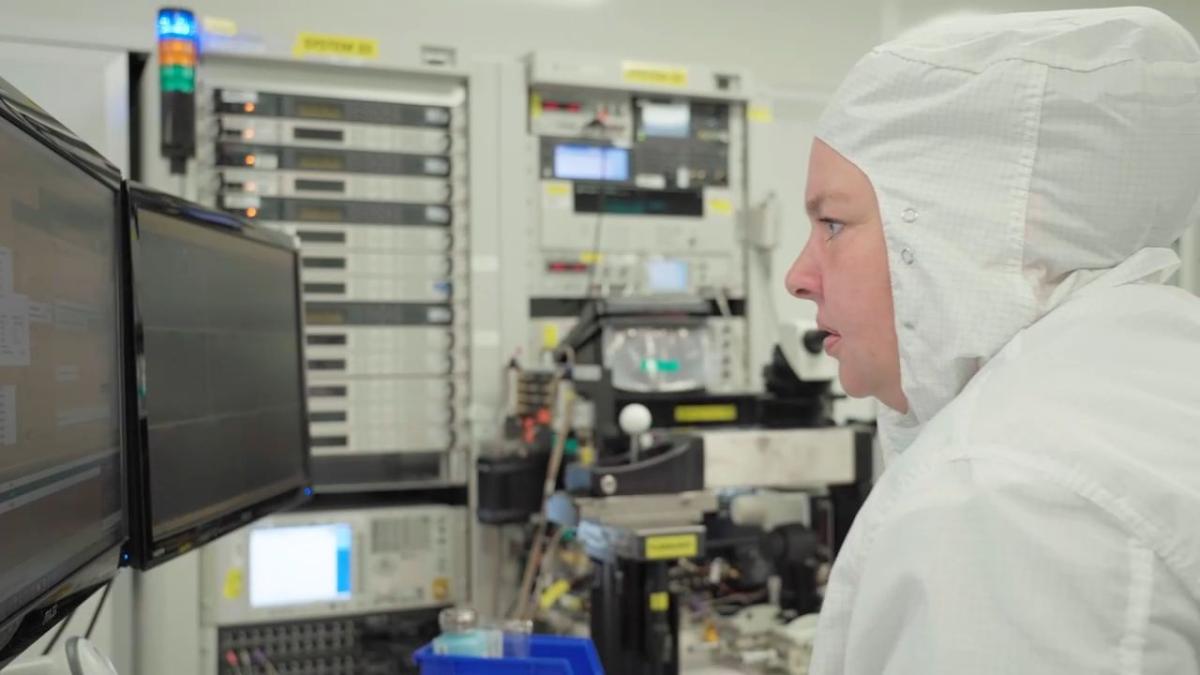 Laura McCarter in a protective suit looking at computer screens.