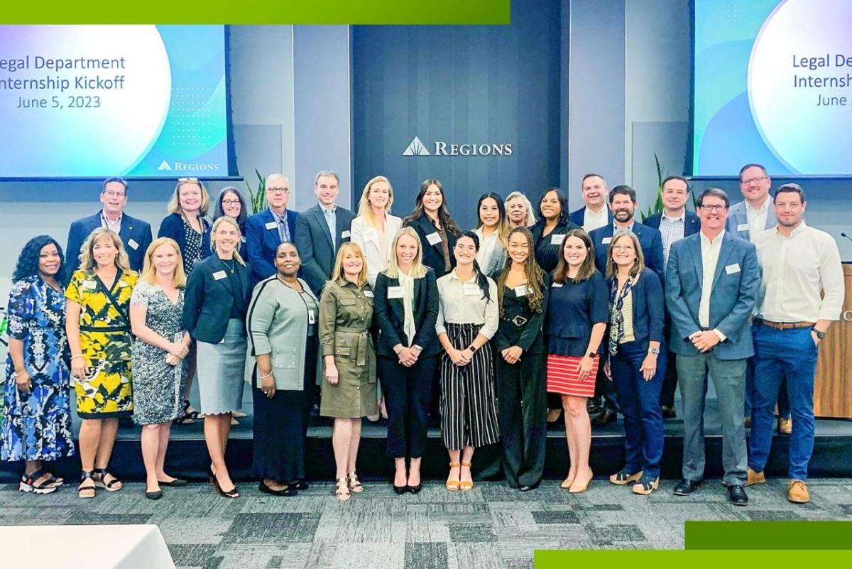 A group of interns and employees posed on a stage. Regions sign and digital screens behind them.