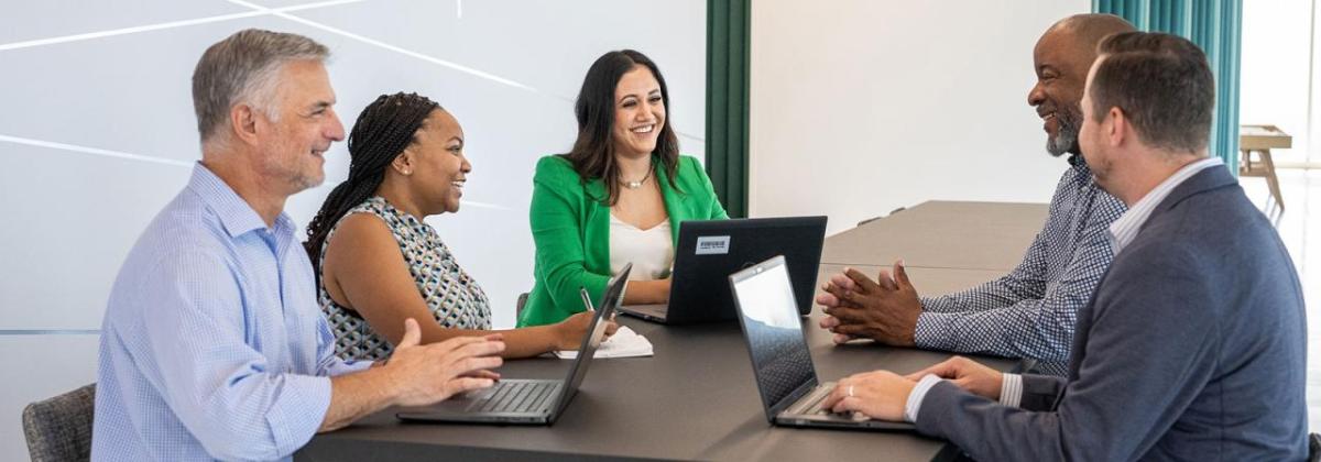 Lesly Luque and team at a conference table, some with open laptops.