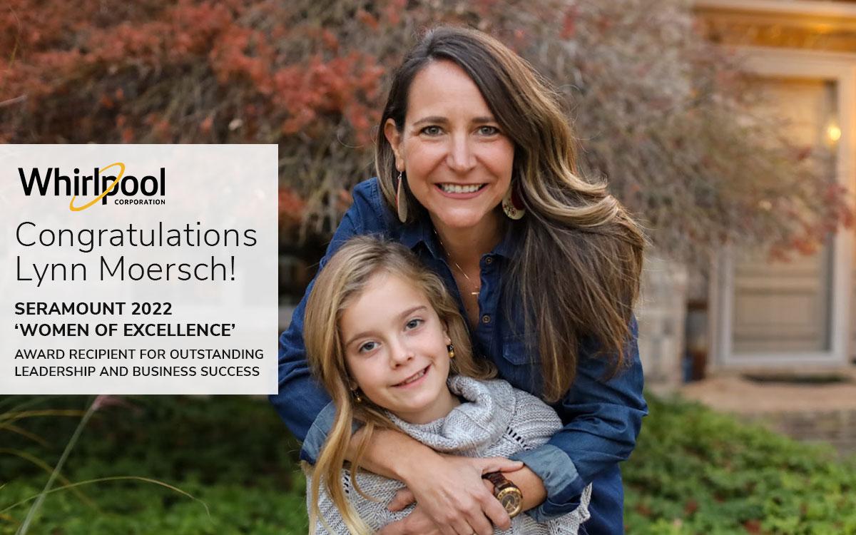 Lynn Moersch hugs a child outside a building with landscaping. "whirlpool- congratulations Lynn Moresch!" on the left.