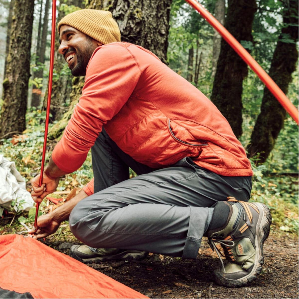 Person in orange jacket setting up a tent in the woods