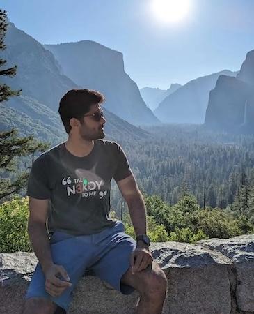 Manoj seated on a wall with a vista of the mountains behind him.