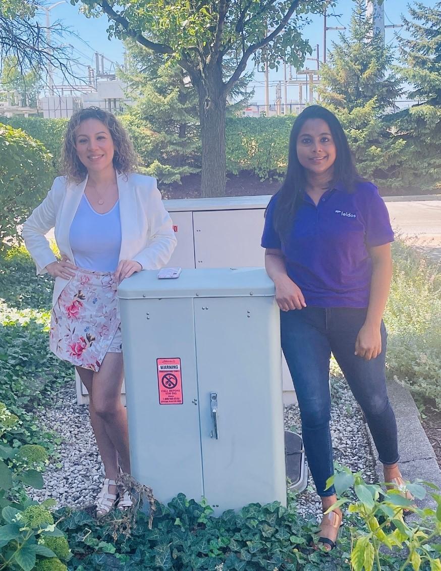 Two people posed next to an outdoor electrical box.