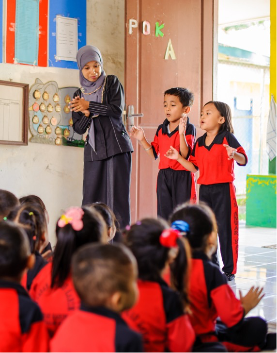 teacher and two students standing in front of sitting class