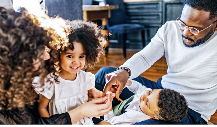 Black family of four seated on the floor of their home.