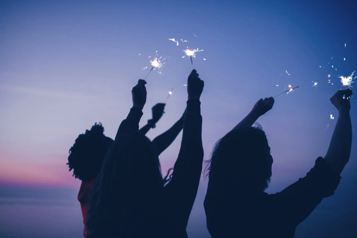 Three people waving sparklers in the dark