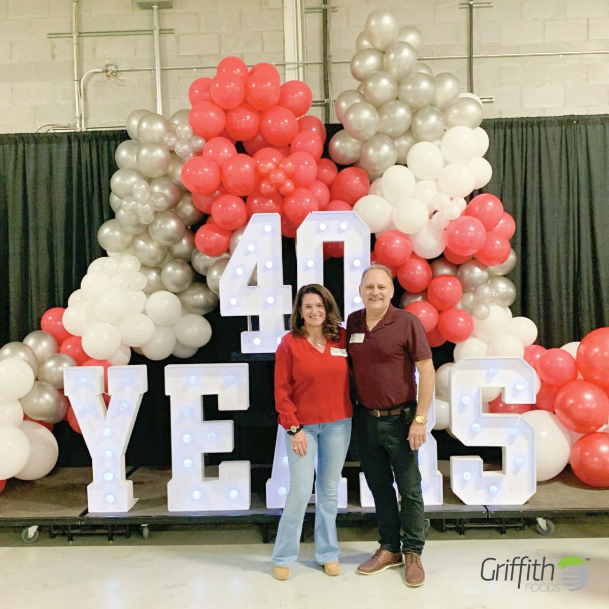 Two people standing in front of balloon display and sign reading "40 Years"