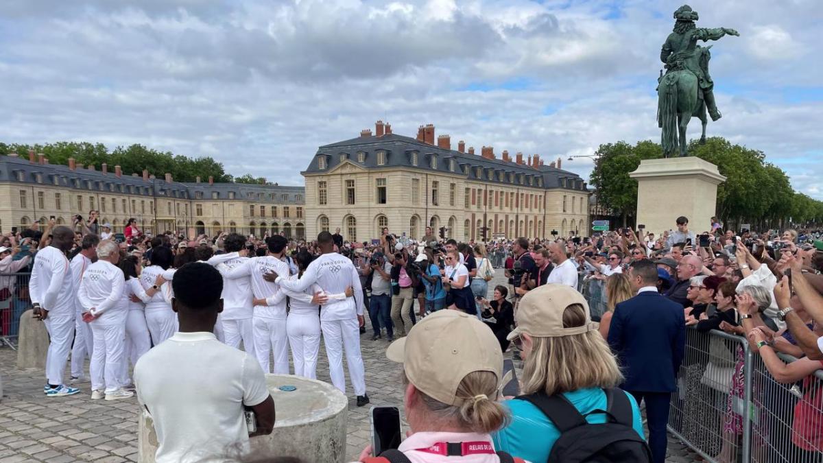 A crowd of people taking photo's of a group of people wearing white Paris 2024 tracksuits