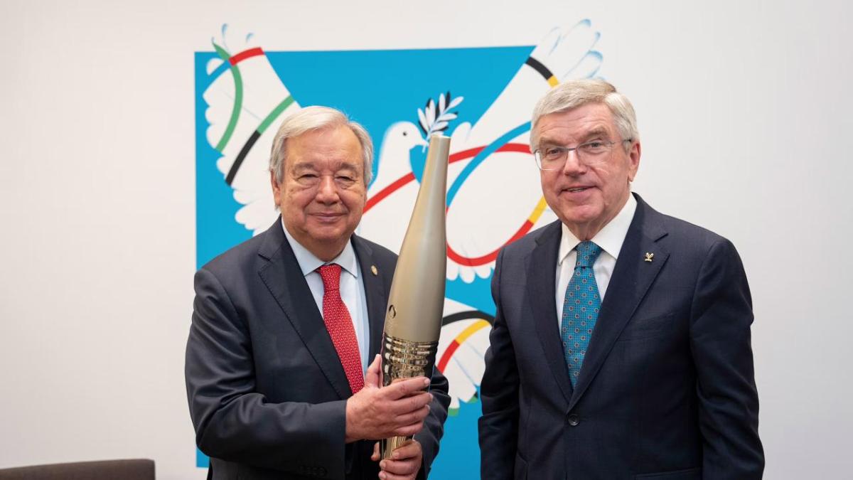 Two people stood next to each other wearing suits, the person on the left is holding the Olympic torch 