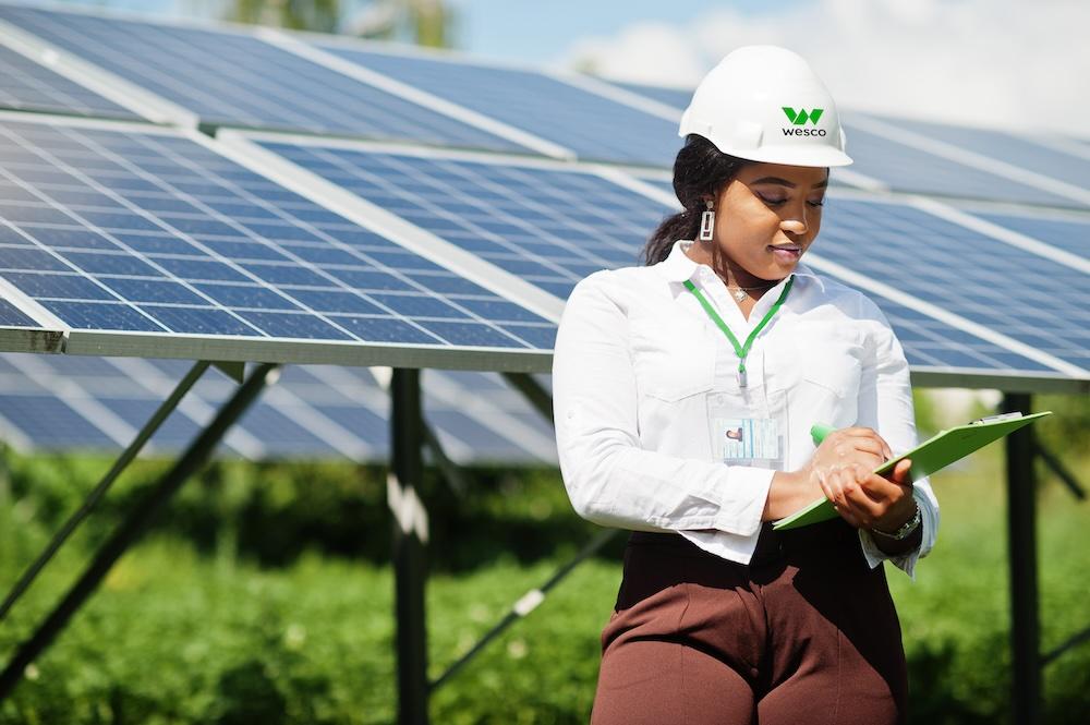 Female Wesco employee shown with a clipboard in front of a solar panel array.