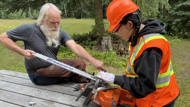 Two people sat on a bench holding a chainsaw