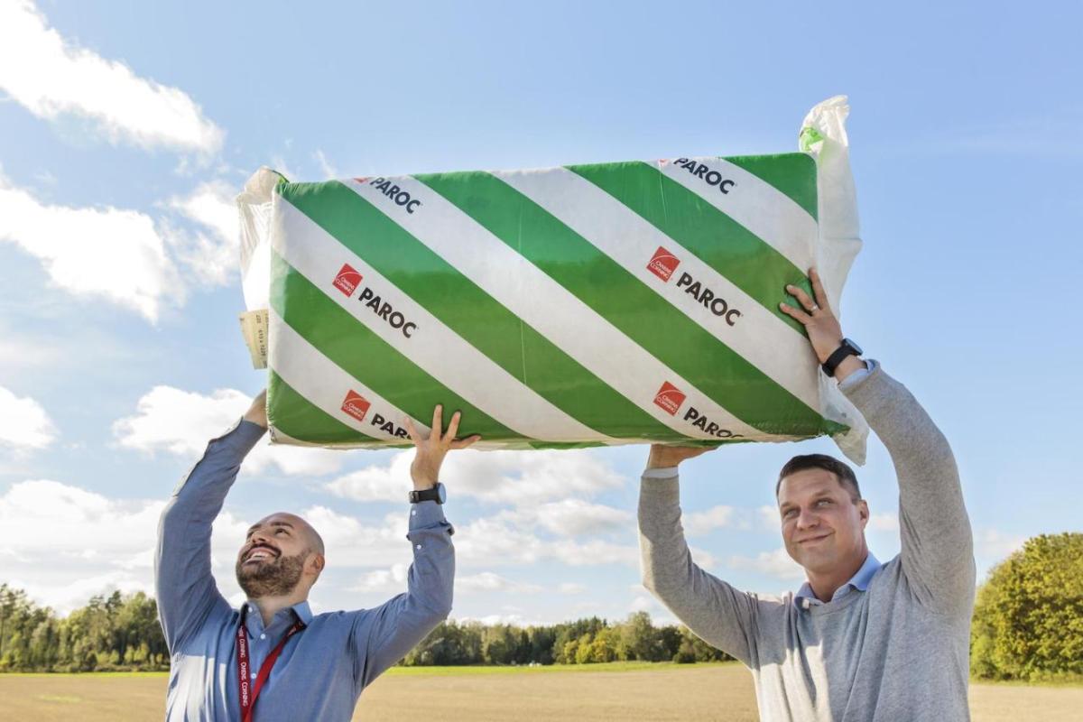 Two people holding up a bat of insulation outside