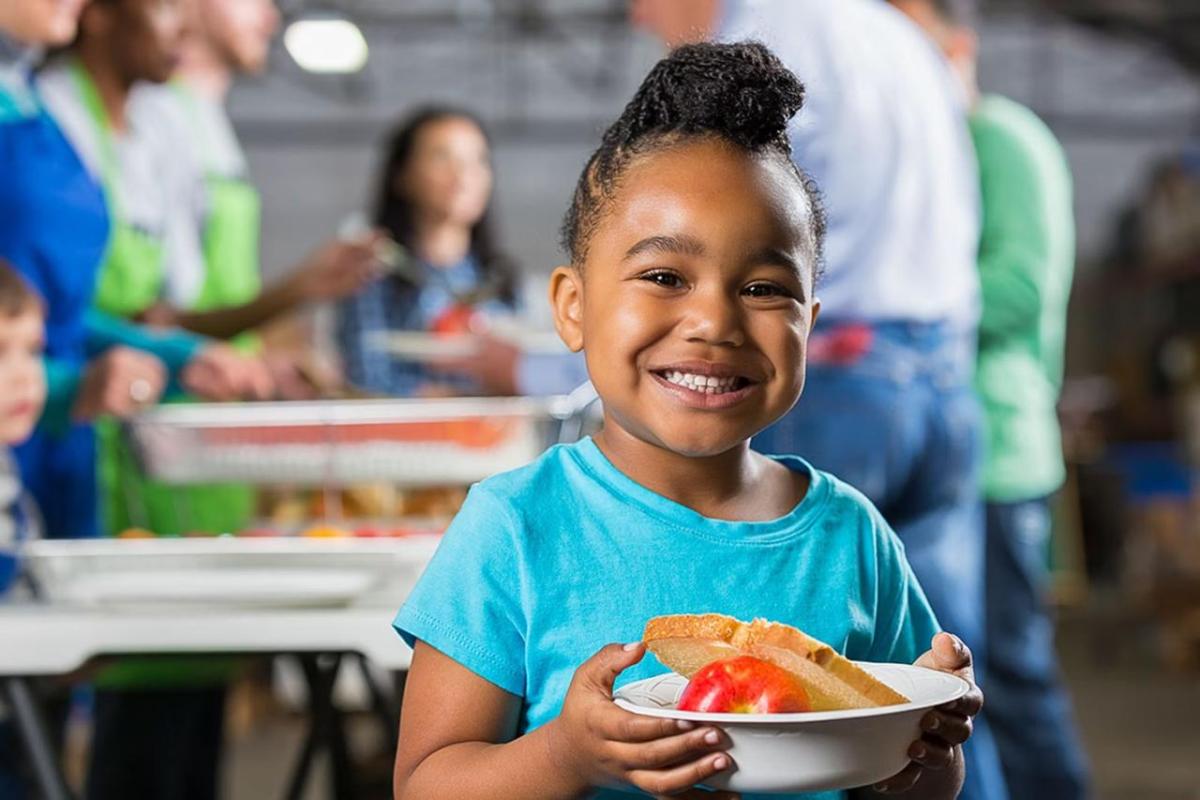 A young child smiling while holding a bowl of food