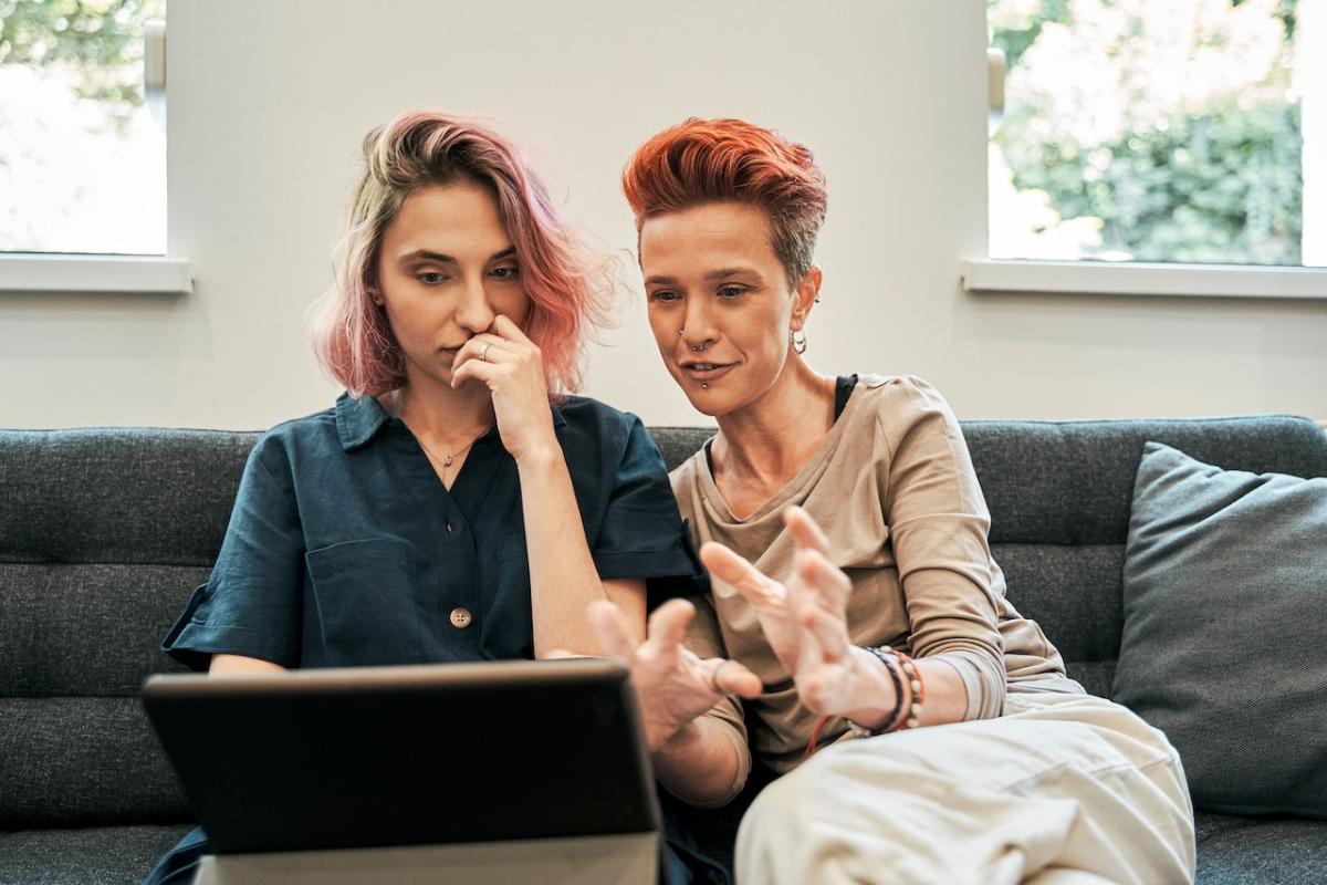 Two people seated on a couch looking at a laptop.